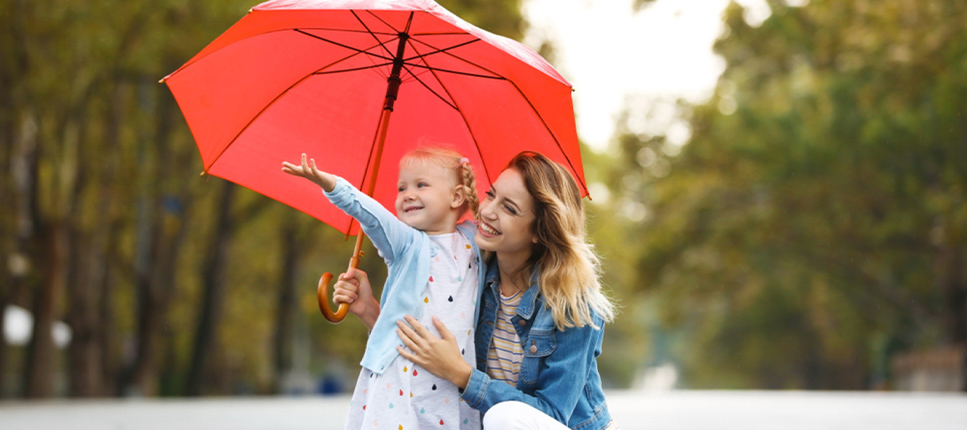 A mother and her young daughter sharing a bright red umbrella on a rainy day