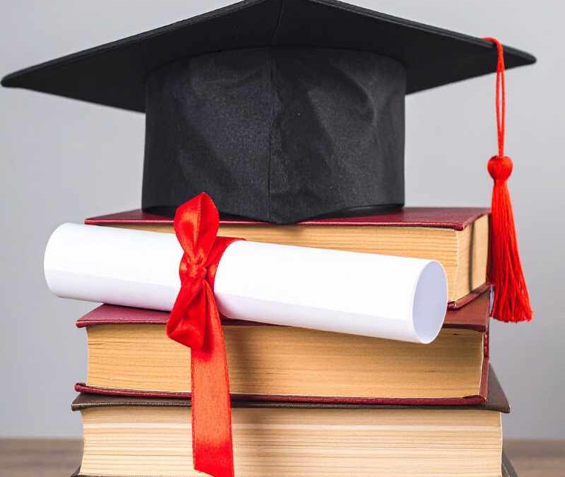 A black graduation cap with a red tassel sits atop a stack of hardcover books, with a rolled diploma tied in a red ribbon tucked between them - btmins.com